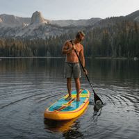 Thumbnail for A surfer paddling a POP Yacht Hopper 11' Inflatable Touring Paddle Board SUP – Turq/Neon/Pink on a calm lake